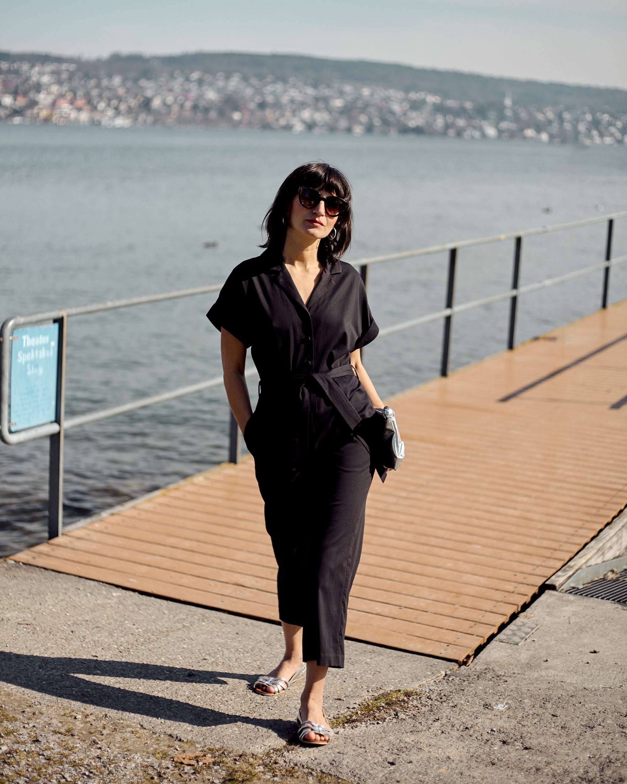 Petite model wearing the Black Jumpsuit in a full-body editorial portrait by the lakeside.