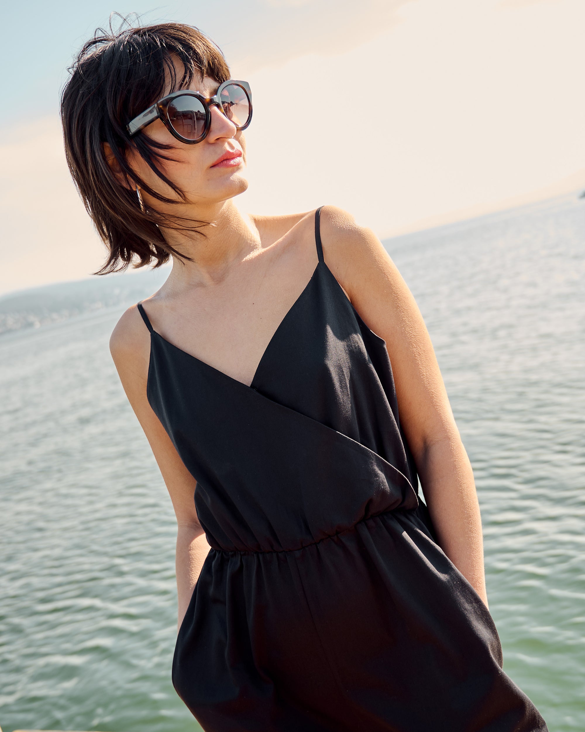 Close-up of model wearing petite black wrap jumpsuit by the lake.