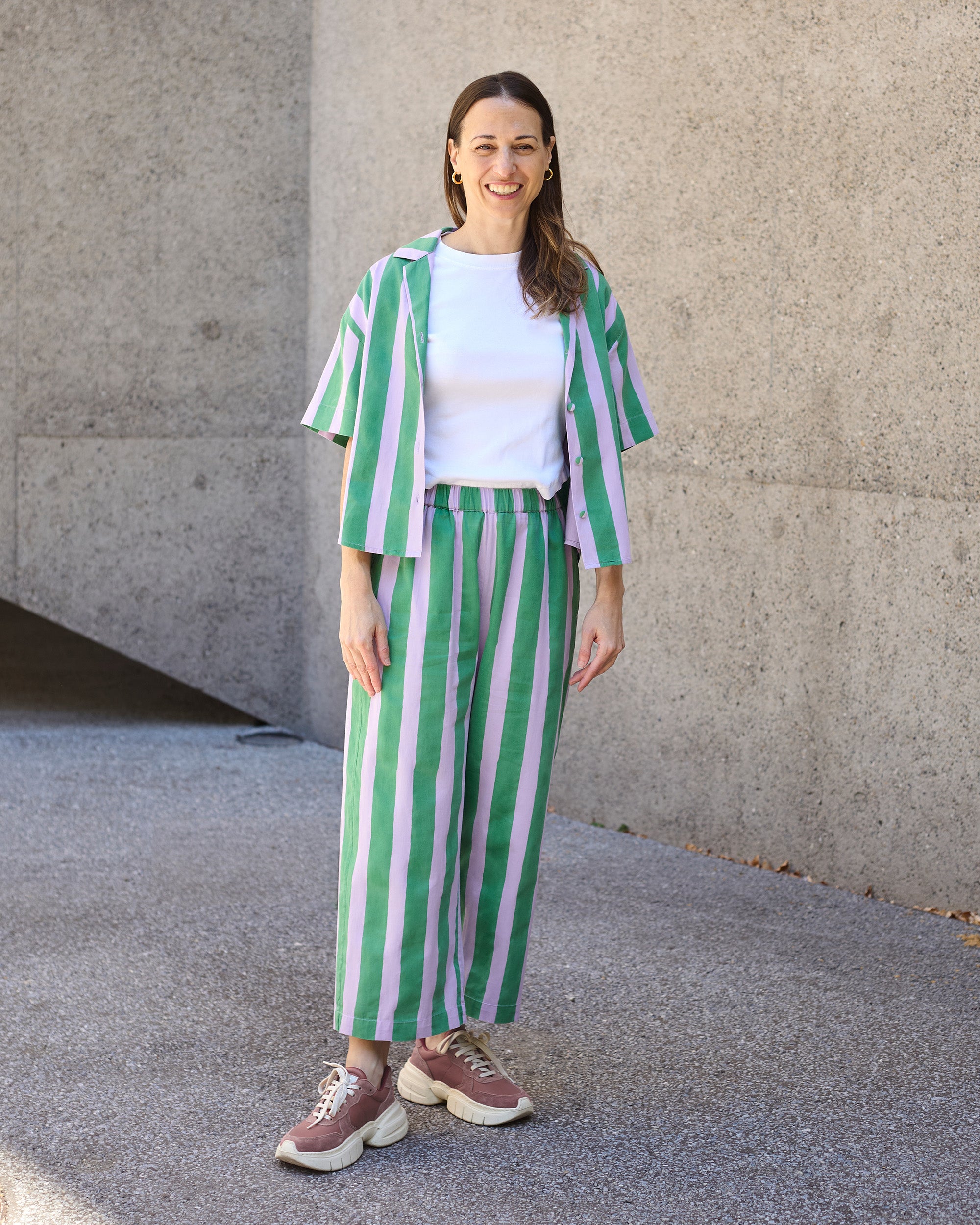 Model wearing petite striped blockprint wide-leg trousers with matching blouse in green and lilac stripes.