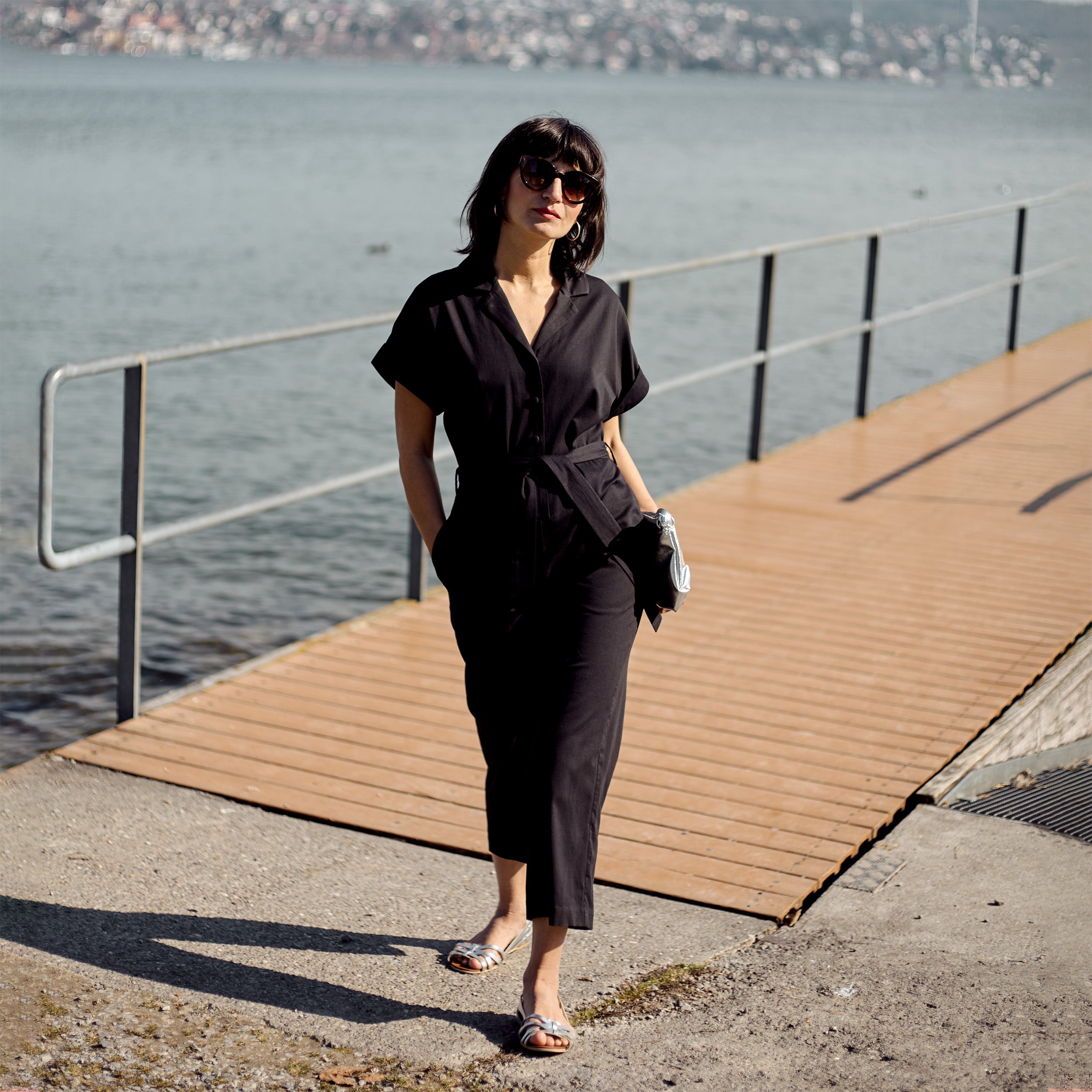 Petite model wearing the Black Jumpsuit in a full-body editorial portrait by the lakeside.
