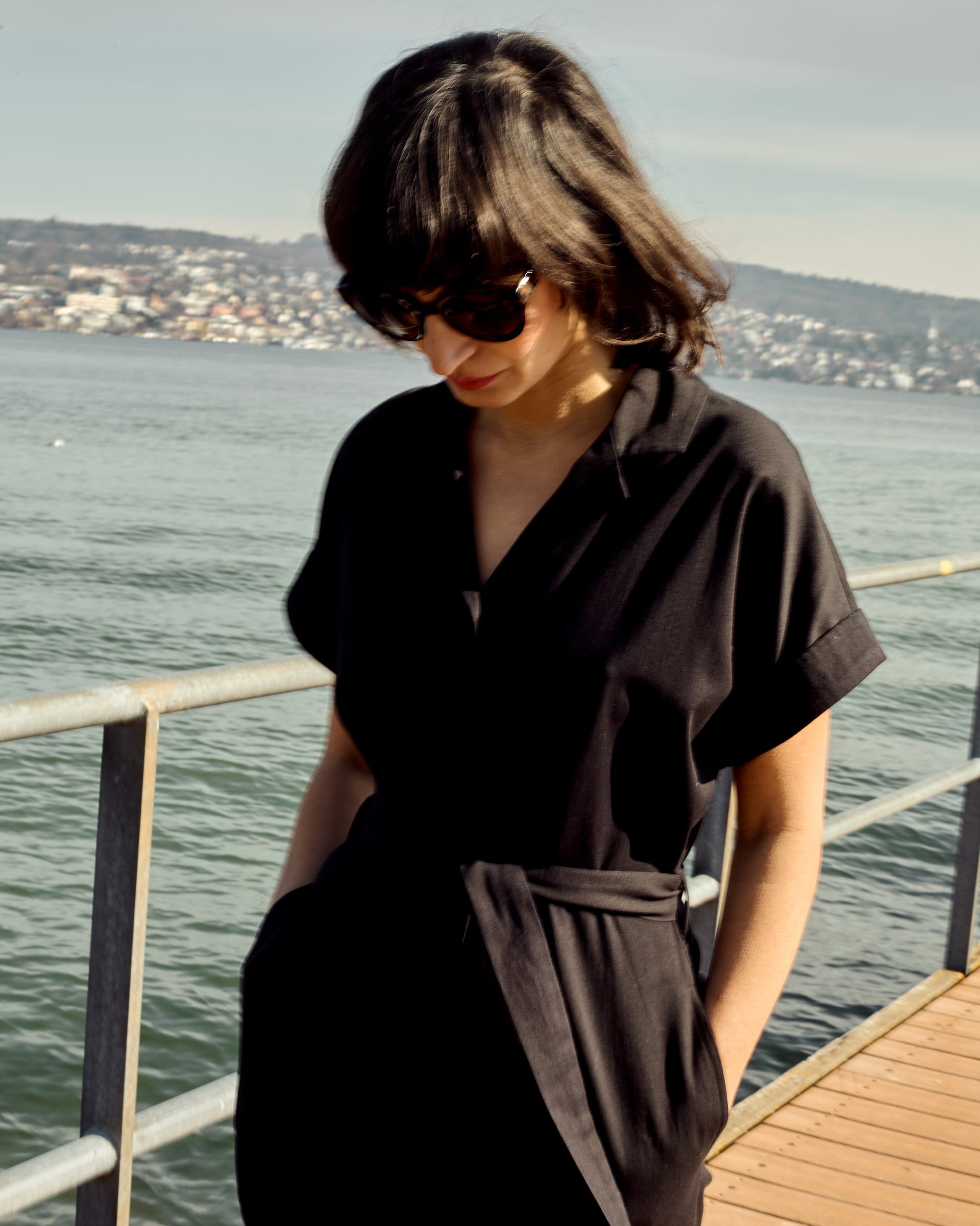 Petite model wearing the Black Jumpsuit with short sleeves and a waist tie by the lakeside.