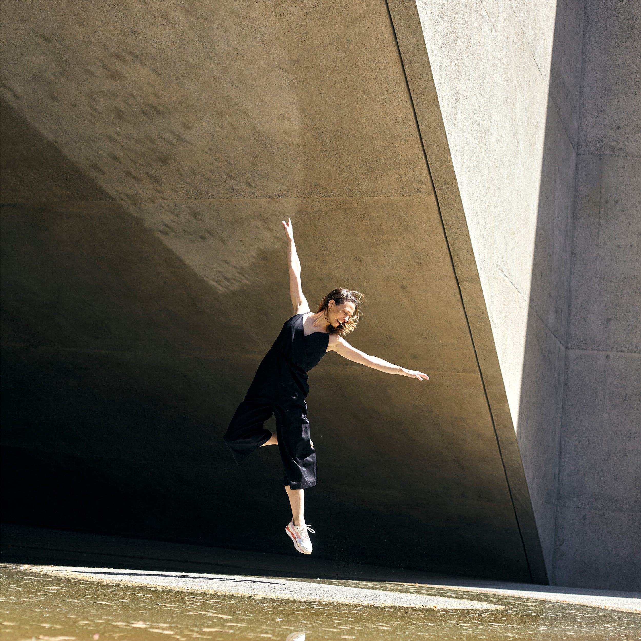Model wearing petite black wrap jumpsuit captured in motion.